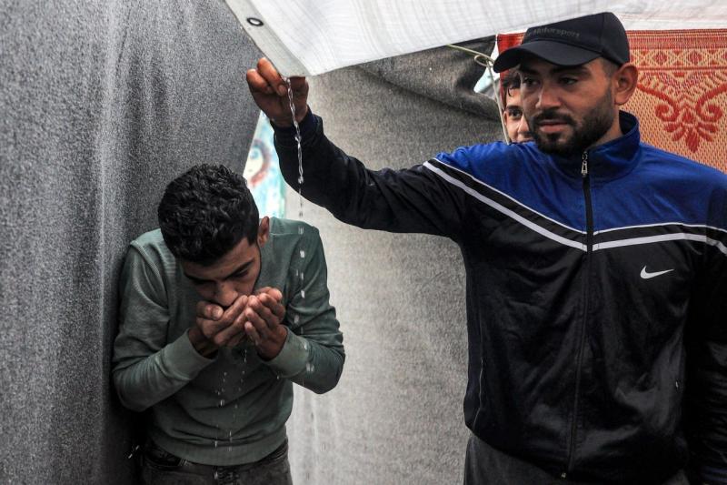 شاب في غزة يشرب الماء من بقايا الأمطار العالقة بالخيمة