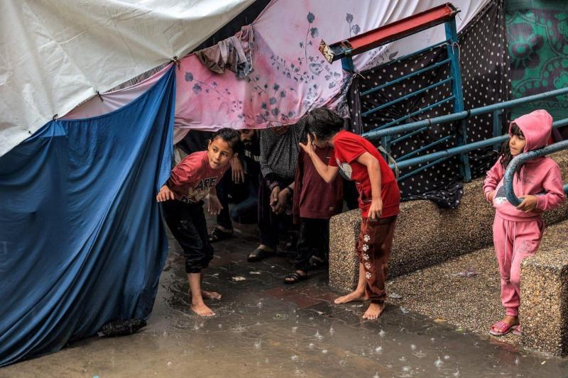 أطفال يحتمون من المطر تحت خيمة في مدرسة تابعة للأونروا في رفح
