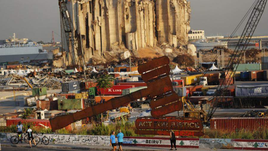 أشخاص يمرون بجوار نصب تذكاري لرمز العدالة يقع أمام صوامع حبوب  تدمرت في انفجار مرفأ بيروت/ اسوشيتدبرس