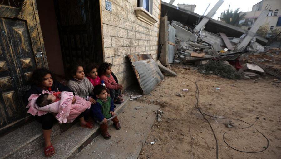 أطفال غزيون يجلسون عند باب بيتهم وحولهم أنقاض جراء قصف الاحتلال
