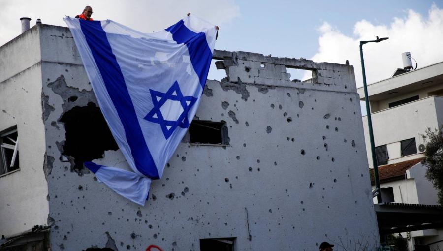 إسرائيليون يعلقون علم الاحتلال الإسرائيلي على مبنى متضرر أصيب بصاروخ من لبنان  في كريات بياليك 22/9/2024 | المصدر: رويترز