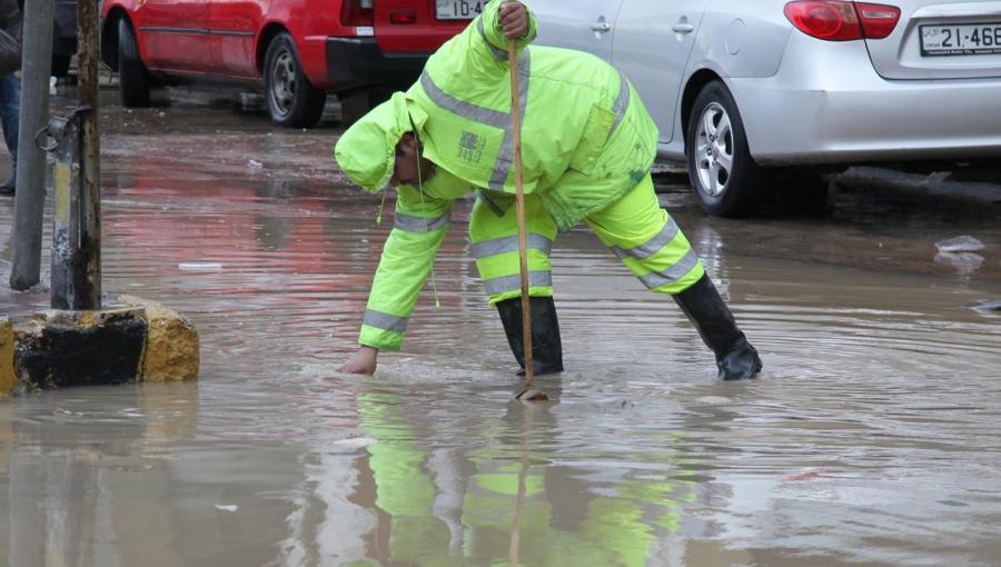 أحد كوادر أمانة عمان يحاول تصريف تجمع للمياه في أحد شوارع العاصمة | بترا