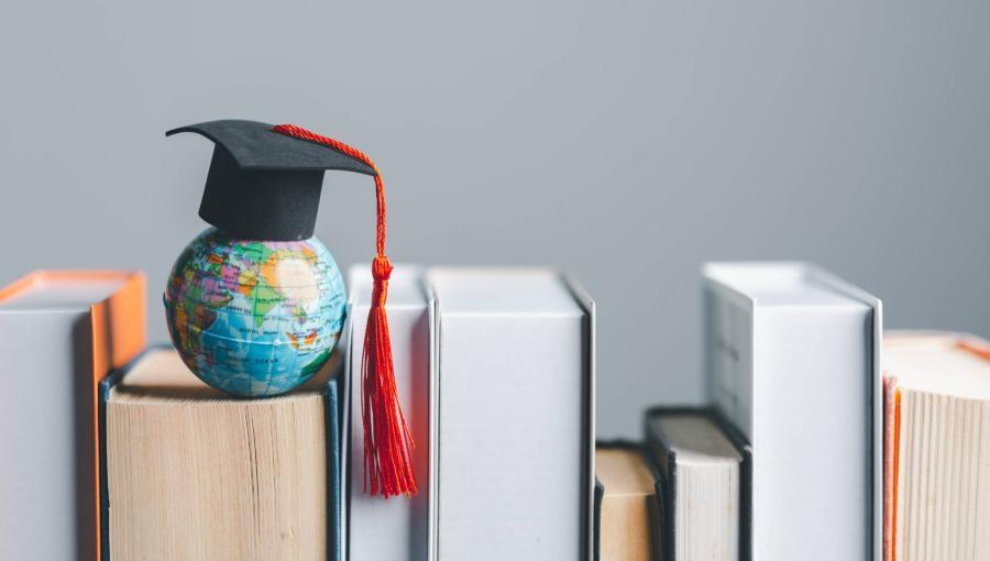 قبعة تخرج تعلو مجسم كرة أرضية وضعت على مجموعة كتب مصفوفة | تعبيرية
