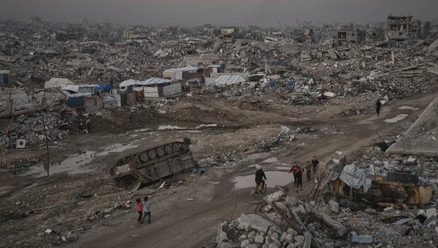 فلسطينيون يمرون قرب عربة مدمرة للاحتلال في مدينة غزة 27/11/2025 | أسوشييتد برس