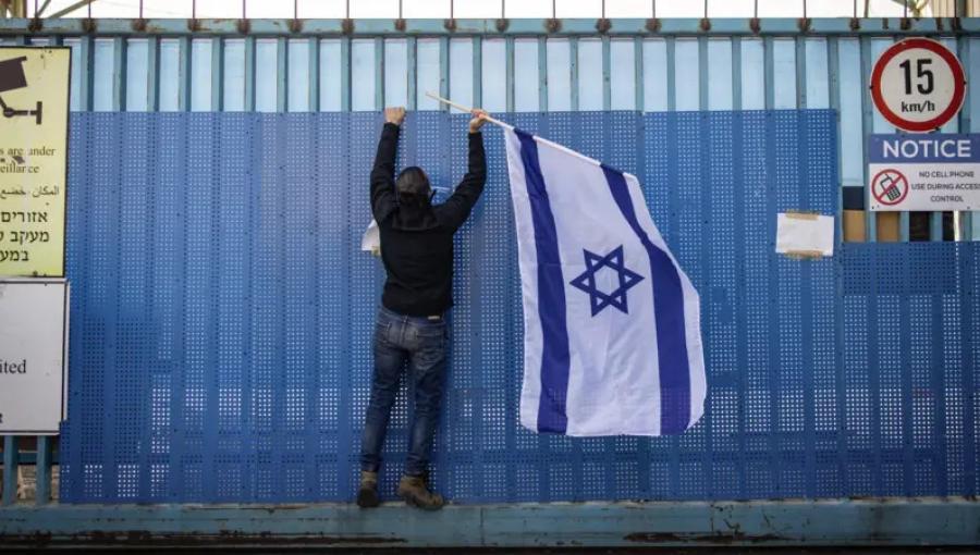 مستوطن يعلق علم الاحتلال على البوابة المغلقة لمبنى وكالة الأونروا في القدس المحتلة 30/1/2025 | المصدر: Getty Images