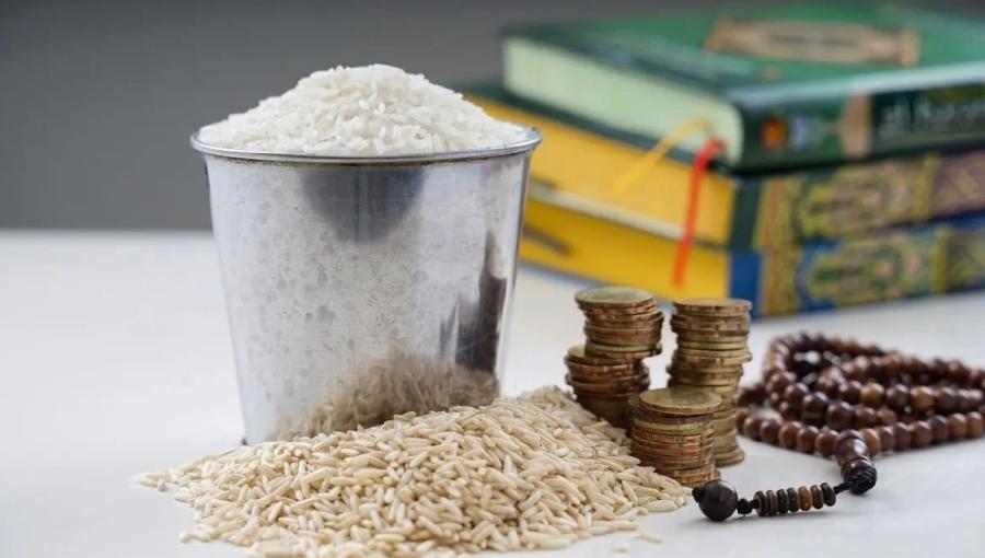 وعاء معدني ممتلئ بحبوب الأرز البيضاء وإلى جانبه نقود معدنية في دلالة على زكاة الفطر