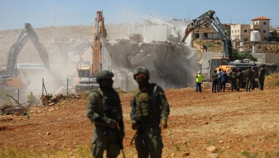 جنديان من جيش الاحتلال يقفان بالقرب من آلية تهدم منزلا بوقت سابق في الضفة الغربية | الأناضول
