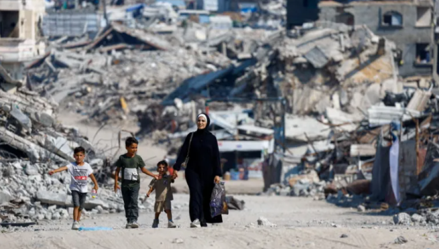 فلسطينيون يسيرون بين أنقاض المباني السكنية التي دمرت خلال العدوان على مدينة غزة | رويترز