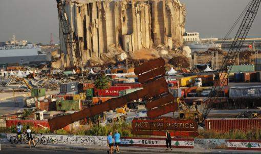 أشخاص يمرون بجوار نصب تذكاري لرمز العدالة يقع أمام صوامع حبوب  تدمرت في انفجار مرفأ بيروت/ اسوشيتدبرس