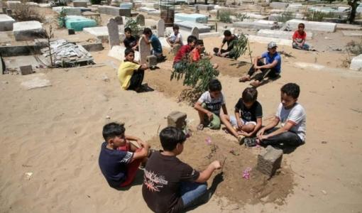 أطفال يجلسون حول قبور الشهداء الخمسة في غزة
