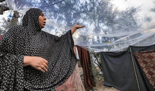 امرأة في غزة تغطي الخيمة بكيس بلاستيكي لحمايتها من المطر