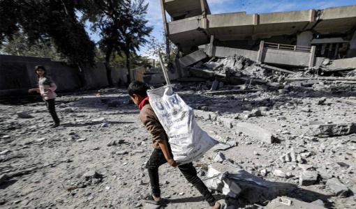 صبي يحمل كيسا جمع فيه حاجياته من أنقاض مدرسة ثانوية دمرها قصف الاحتلال في مخيم النصيرات في غزة | وكالة الأنباء الفرنسية