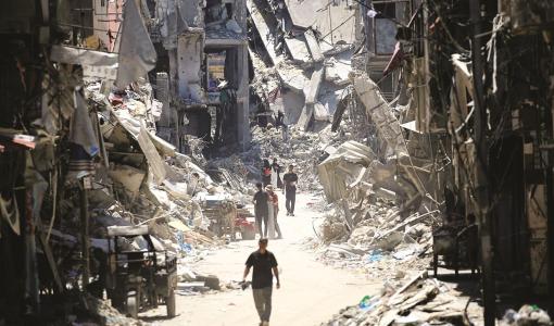 فلسطينيون يسيرون بجوار مبان مدمرة في خانيونس جنوب قطاع غزة | المصدر: وكالة الأنباء الفرنسية