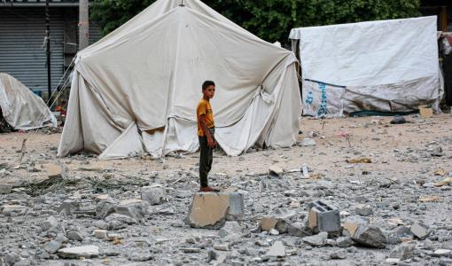 شاب فلسطيني يقف أمام خيمة في منطقة دير البلح وسط الحطام الذي تسبب به قصف الاحتلال | المصدر: وكالة الأنباء الفرنسية