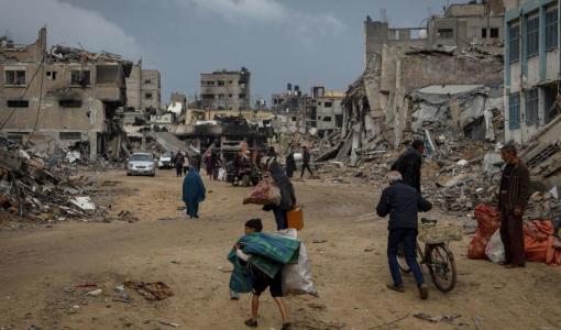 فلسطينيون يسيرون في مدينة خانيونس جنوب قطاع غزة بين مبان مهدمة وهم يحملون متعلقاتهم بحثا عن الأمان| المصدر: الأمم المتحدة