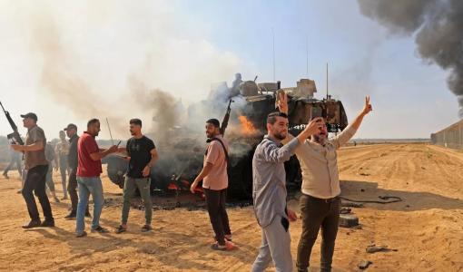 فلسطينيون يحتفلون باستيلائهم على دبابة إسرائيلية بالقرب من خانيونس بعد عبور السياج الفاصل بين دولة الاحتلال وقطاع غزة 7 أكتوبر/تشرين الأول 2023 | المصدر: وكالة فرانس برس