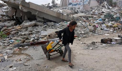 فتاة فلسطينية تنقل المياه النظيفة أثناء سيرها بجوار مبنى مدمر في مدينة غزة، 2/11/2024|المصدر:وكالة الصحافة الفرنسية