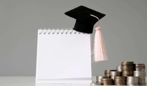 دفتر فوقه قبعة تخرج بجانبه نقود | تعبيرية