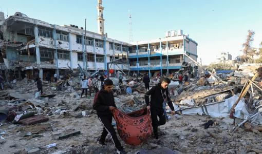 فلسطينيان يحملان جثة شهيد في مدرسة أبو هميسة | المصدر: وكالة الأنباء الفرنسية