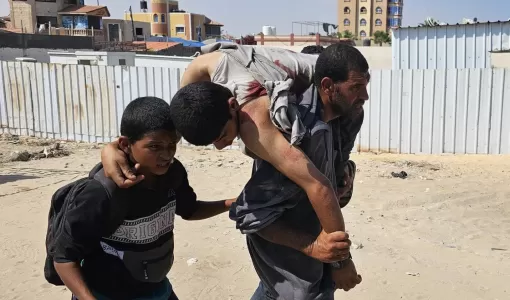 فلسطيني يحمل رجلا أصيب في أثناء وقوفه في طابور للحصول على مساعدات | المصدر: وكالة الأنباء الفرنسية