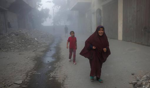 فلسطينية تفر بعيدا عن موقع غارة إسرائيلية استهدفت مبنى سكنيا غرب جباليا شمال قطاع غزة 27/8/2025 | المصدر: وكالة الأنباء الفرنسية