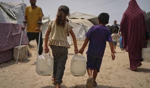 طفلان يتساعدان لحمل وعائي ماء في مدينة غزة 12/8/2025 | المصدر: أسوشييتد برس