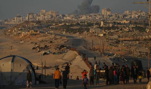 فلسطينيون يسيرون على طول الطريق الساحلي وفي الخلفية دخان يتصاعد إلى السماء بعد غارة شنها الاحتلال على مدينة غزة | أسوشييتد برس