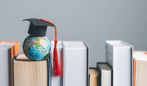 قبعة تخرج تعلو مجسم كرة أرضية وضعت على مجموعة كتب مصفوفة | تعبيرية