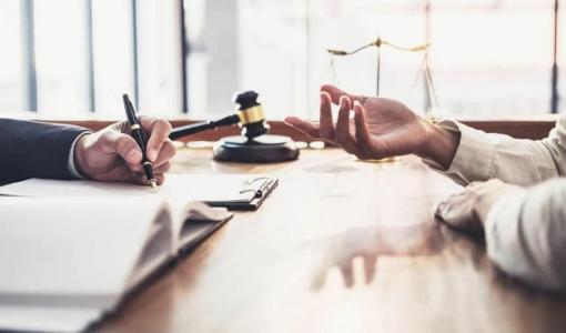 شخصان على طاولة أمام أوراق رسمية مع مطرقة قاض وميزان العدالة في دلالة على المطالبة بالحقوق | تعبيرية