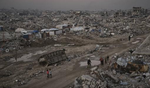 فلسطينيون يمرون قرب عربة مدمرة للاحتلال في مدينة غزة 27/11/2025 | أسوشييتد برس