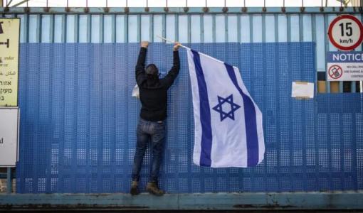 مستوطن يعلق علم الاحتلال على البوابة المغلقة لمبنى وكالة الأونروا في القدس المحتلة 30/1/2025 | المصدر: Getty Images