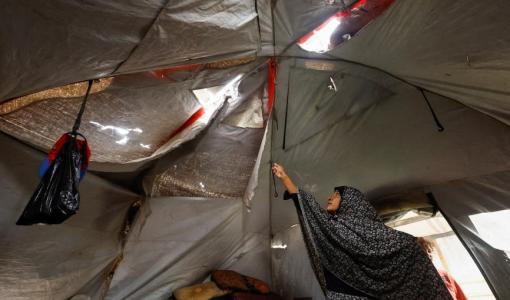 سيدة فلسطينية تعرض سقف خيمتها الممزق في أحد مخيمات النزوح في قطاع غزة | رويترز