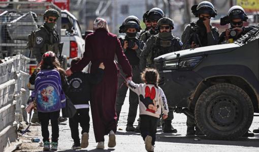 فلسطينية بصحبة أطفال يمرون قرب قوات الاحتلال الإسرائيلية التي اقتحمت حي كفر عقب قرب رام الله في الضفة الغربية 26/1/2026 | وكالة الأنباء الفرنسية