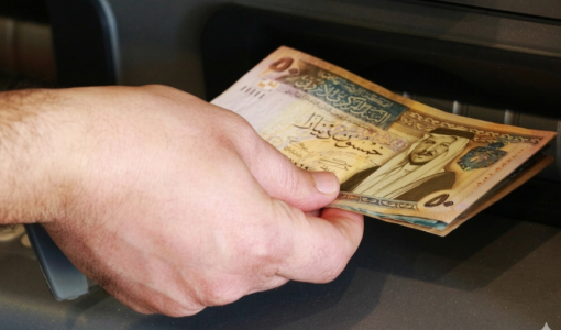 شخص يمسك مبلغا ماليا يخرج من جهاز الصراف الآلي