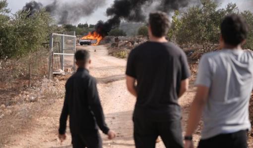 فلسطينيون يقفون بالقرب من مركبة تحترق جراء اعتداء سابق للمستوطنين | الأناضول