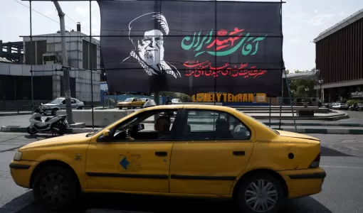 سيارة أجرة تمر أمام لافتة تحمل صورة المرشد الإيراني السابق علي خامنئي قبيل جنازته في طهران | رويترز