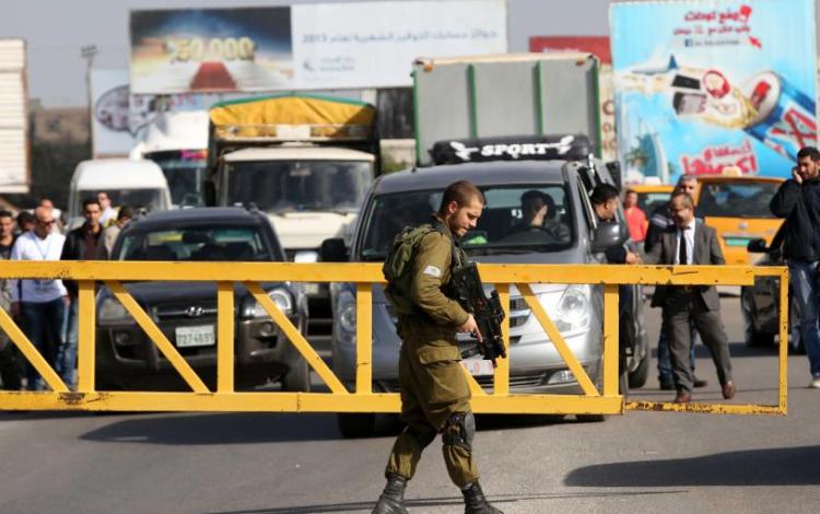 جندي إسرائيلي يقف أمام حاجز عسكري ويمنع مركبات الفلسطينيين من العبور