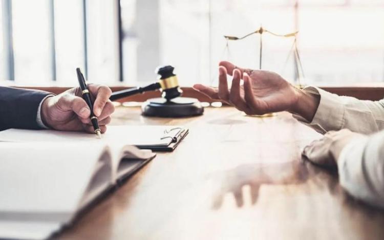 شخصان على طاولة أمام أوراق رسمية مع مطرقة قاض وميزان العدالة في دلالة على المطالبة بالحقوق | تعبيرية