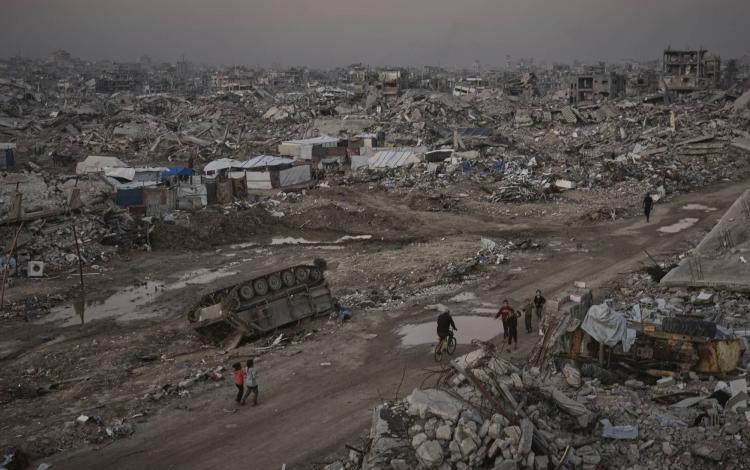 فلسطينيون يمرون قرب عربة مدمرة للاحتلال في مدينة غزة 27/11/2025 | أسوشييتد برس