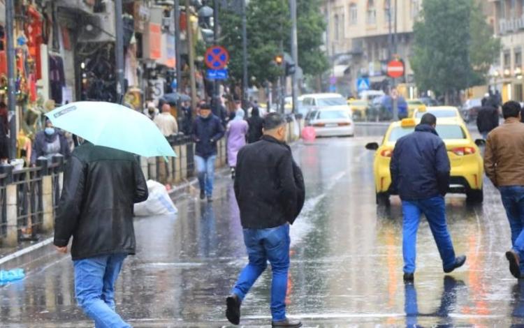 مشهد شتوي من أحد شوارع العاصمة عمان، حيث يسير الناس تحت المطر، بعضهم يحمل مظلات