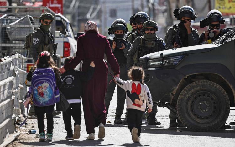 فلسطينية بصحبة أطفال يمرون قرب قوات الاحتلال الإسرائيلية التي اقتحمت حي كفر عقب قرب رام الله في الضفة الغربية 26/1/2026 | وكالة الأنباء الفرنسية