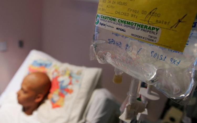 كيس علاج كيميائي معلق في غرفة مستشفى، بينما يبدو في الخلفية مريض سرطان مستلقٍ على السرير | Getty Images