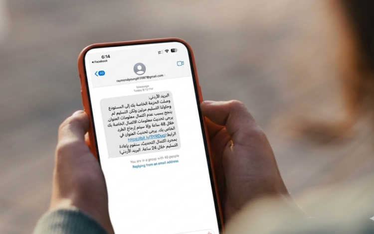 شخص يحمل هاتفا وتظهر عليه رسالة احتيالية باسم البريد الأردني