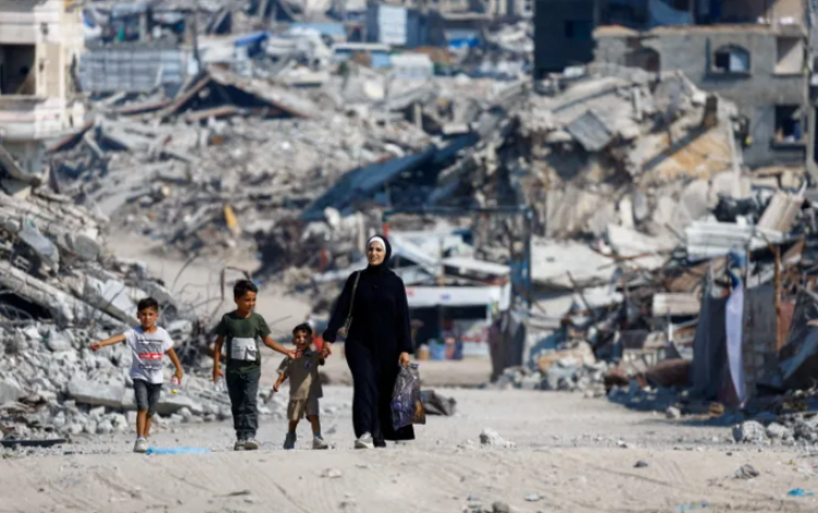 فلسطينيون يسيرون بين أنقاض المباني السكنية التي دمرت خلال العدوان على مدينة غزة | رويترز